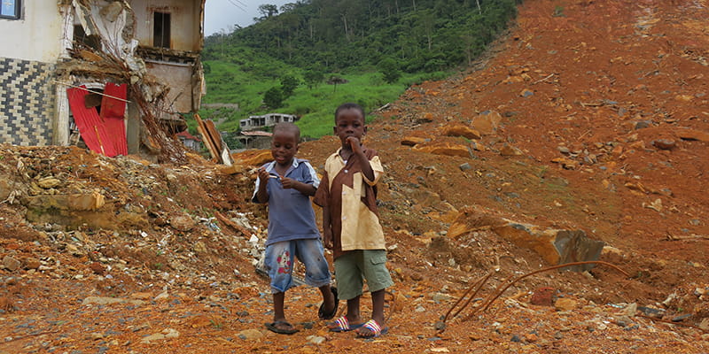 Kinder in Trümmern vor kapputem Haus